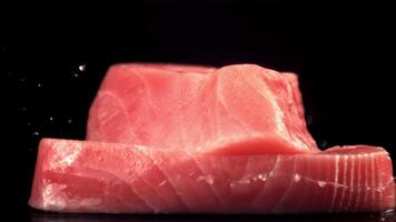 The super slow motion raw tuna steak falls on the second piece on the table. On a black background. Filmed on a high-speed camera at 1000 fps. video