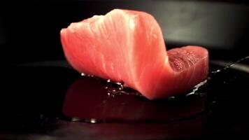 Super slow motion raw tuna steak falls on a pan with a splash of oil. On a black background.Filmed on a high-speed camera at 1000 fps. video