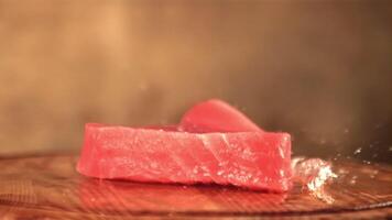 Super schleppend Bewegung frisch Thunfisch Steak Stürze auf ein Schneiden Tafel mit spritzt von Wasser. auf ein braun Hintergrund. gefilmt auf ein schnelle Geschwindigkeit Kamera beim 1000 fps. video