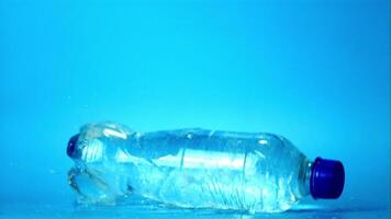 Super slow motion with splashes on the table drops a bottle of water. Filmed on a high-speed camera at 1000 fps.On a blue background. video