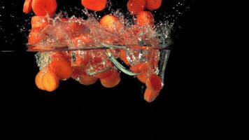 Super slow motion pieces of carrot fall into the water with splashes. On a black background. Filmed on a high-speed camera at 1000 fps. High quality FullHD footage video