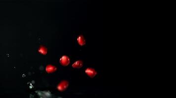 Super slow motion pomegranate grains fall into the water with splashes. On a black background. Filmed on a high-speed camera at 1000 fps.High quality FullHD footage video