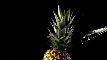 super langzaam beweging Aan een roterend ananas druppels een Jet van water. Aan een zwart achtergrond.gefilmd Aan een hoge snelheid camera Bij 1000 fps. video