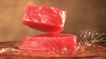 Super schleppend Bewegung mit spritzt von Wasser fallen Thunfisch Steaks auf ein hölzern Schneiden Tafel. auf ein braun Hintergrund. gefilmt auf ein schnelle Geschwindigkeit Kamera beim 1000 fps. video