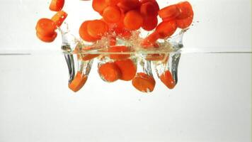 Super slow motion sliced carrots fall into the water with splashes and air bubbles. On a white background. Filmed on a high-speed camera at 1000 fps. High quality FullHD footage video