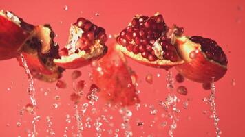 Super slow motion pieces of pomegranate with splashes of water. On a red background. Filmed on a high-speed camera at 1000 fps. High quality FullHD footage video