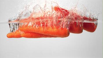 Super slow motion ripe carrots with spray falls into the water. On a white background. Filmed on a high-speed camera at 1000 fps. High quality FullHD footage video