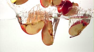 Super slow motion pieces of ripe apple fall into the water with splashes. On a white background.Filmed on a high-speed camera at 1000 fps. High quality FullHD footage video