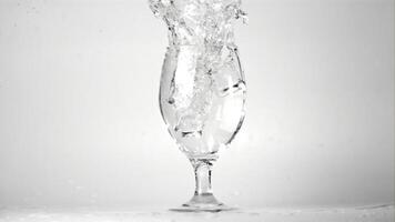 súper lento movimiento hielo caídas dentro un vaso de agua con rociar. en un blanco antecedentes. filmado a 1000 fps. video