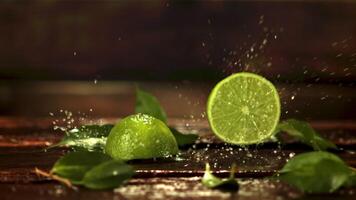 Super slow motion halves of lime fall on the table with splashes of water. Filmed at 1000 fps.On a wooden background. video