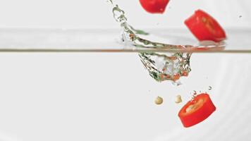 super långsam rörelse hackad chili peppar falls in i de vatten med stänk. på en vit bakgrund. hög kvalitet full HD antal fot video
