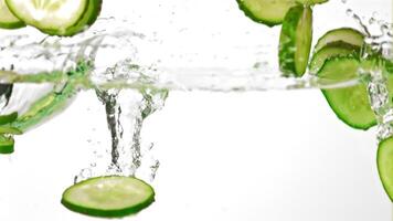 Super slow motion pieces of fresh cucumbers fall into the water with splashes. On a white background.Filmed on a high-speed camera at 1000 fps. High quality FullHD footage video