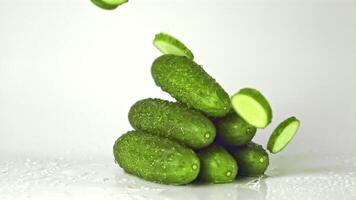 Super slow motion pieces of cucumber fall on a bunch of cucumbers on the table. On a white background. Filmed on a high-speed camera at 1000 fps. High quality FullHD footage video