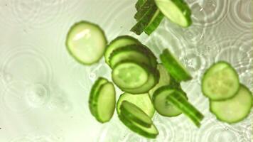 Super slow motion chopped cucumber falls on water with spray. On a white background. Filmed on a high-speed camera at 1000 fps. High quality FullHD footage video