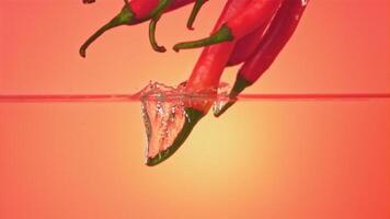 Super slow motion chilli pepper falls into the water with splashes. On a pink background. Filmed on a high-speed camera at 1000 fps. High quality FullHD footage video