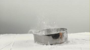 súper lento movimiento en el mesa con harina que cae tamiz. en un blanco antecedentes. filmado en un alta velocidad cámara a 1000 fps. video