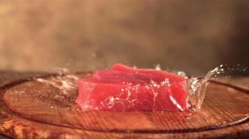 Super schleppend Bewegung auf ein hölzern Schneiden Tafel Stürze roh Thunfisch Steak mit sprühen. auf ein braun Hintergrund. gefilmt auf ein schnelle Geschwindigkeit Kamera beim 1000 fps. video