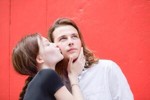 A couple is enjoying a summer vacation in the red wall background, happily showing their love to each other. photo