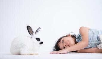 sonriente pequeño niña y con su amado mullido conejo, exhibiendo el belleza de amistad Entre humanos y animales foto