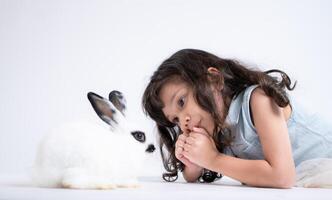 un pequeño niña Besos su amado mullido conejo, el belleza de amistad Entre humanos y animales foto