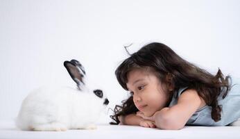 un pequeño niña Besos su amado mullido conejo, el belleza de amistad Entre humanos y animales foto