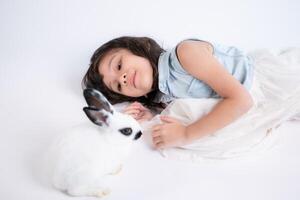 un pequeño niña Besos su amado mullido conejo, el belleza de amistad Entre humanos y animales foto