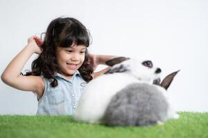 sonriente pequeño niña y con su amado mullido conejo, exhibiendo el belleza de amistad Entre humanos y animales foto