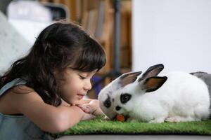 sonriente pequeño niña y con su amado mullido conejo, exhibiendo el belleza de amistad Entre humanos y animales foto