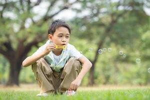 Boy sitting in the park with blowing air bubble, Surrounded by greenery and nature photo