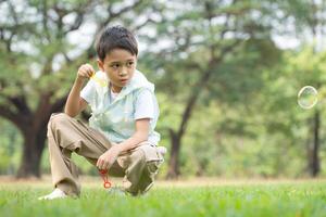 Boy sitting in the park with blowing air bubble, Surrounded by greenery and nature photo