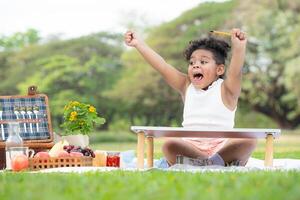 contento familia disfrutando un picnic en el parque, niña son teniendo divertido dibujo en papel metido en el mesa. foto