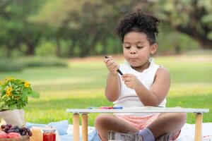 contento familia disfrutando un picnic en el parque, niña son teniendo divertido dibujo en papel metido en el mesa. foto