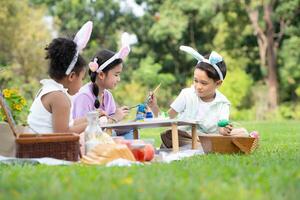 contento familia disfrutando un picnic en el parque, niños sentado y colorante su hermosa Pascua de Resurrección huevos. foto