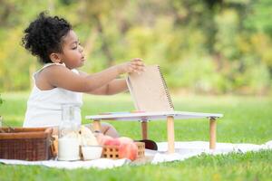 contento familia disfrutando un picnic en el parque, niña son teniendo divertido dibujo en papel metido en el mesa. foto