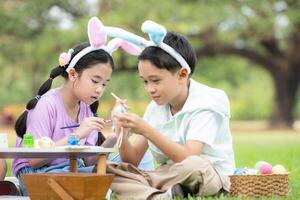 contento familia disfrutando un picnic en el parque, niños sentado y colorante su hermosa Pascua de Resurrección huevos. foto