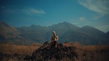 solitario escursionista riposo su un' roccia con panoramico montagna fondale sotto un' chiaro blu cielo. video