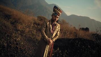 Man in traditional attire standing in a field with mountains in the background. video