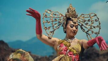 Woman in traditional Balinese costume with ornate headdress, performing a dance with a mountainous backdrop. video