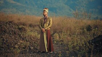 Traditional attire of a man standing in a field with mountains in the background at dusk. video