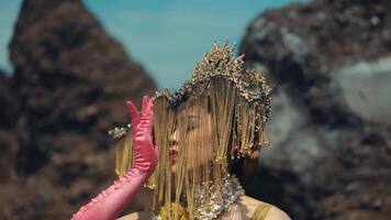 Woman in ornate headpiece and pink gloves posing artistically with a blurred rocky background. video