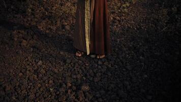 Close-up of a person's feet on a rocky surface, wearing sandals and a flowing brown skirt, with a mysterious and moody atmosphere. video