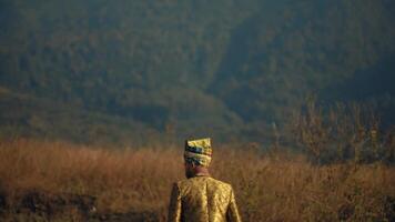 homme dans traditionnel tenue à la recherche en dehors plus de une champ à crépuscule, avec chaud d'or lumière et doux concentrer Contexte. video