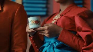 elegante mulher dentro vermelho vestir segurando uma decorativo xícara, com uma foco em a mãos e a copo. video