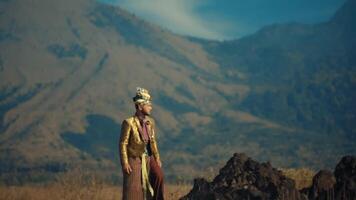 Man in traditional attire standing against mountain backdrop. video