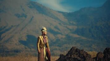 Man in traditional attire standing against mountain backdrop. video