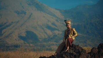 Man in traditional attire sitting on rocks with a majestic mountain in the background. video