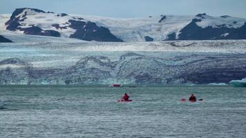 Kayakers move through a melting glacier lagoon at Jokulsarlon, Iceland. 4K video