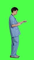 Profile Confident hospital nurse taking notes for the next medic appointment, standing over greenscreen backdrop. Medical assistant with uniform writing patient information on clipboard papers. Camera A. video