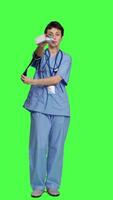 Front view Medical assistant showing tonometer used to measure arterial blood pressure, standing against greenscreen backdrop. Nurse working with sphygmomanometer tool to take measurement at checkup. Camera A. video