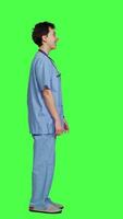 Profile Joyful medical assistant greeting patients with a smile and waving, saying hello in studio against greenscreen backdrop. Smiling cheerful nurse welcoming people at healthcare clinic. Camera A. video